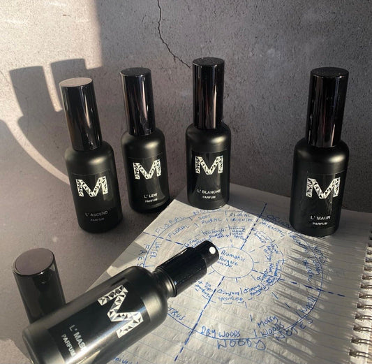 5 Bottles of L'Scents Parfum an organic hand made perfume by Malano sitting ontop of a perfume scents chart, softly lit by sunlight agains a light concrete background.