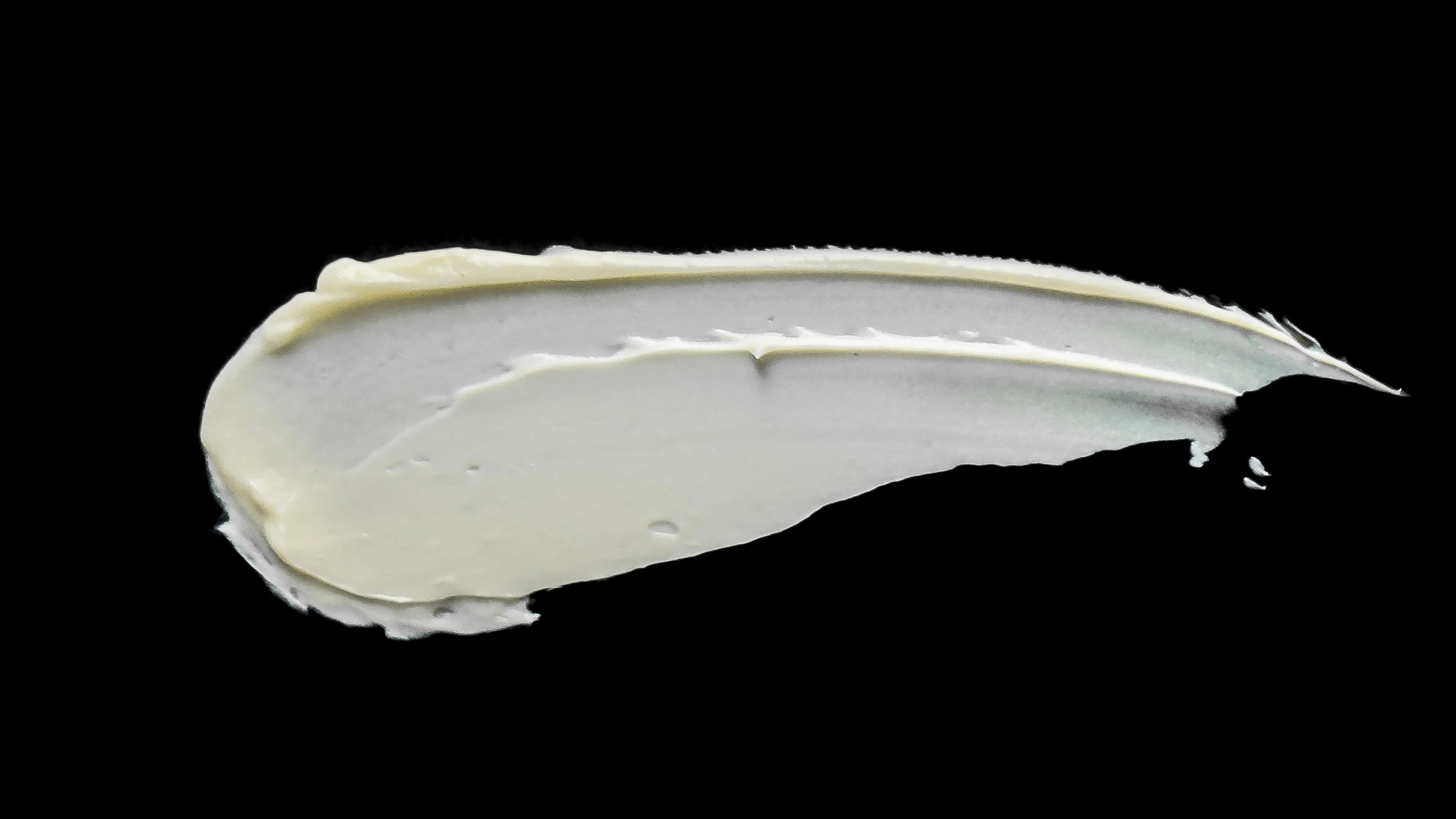 A swatch of creamy organic moisturiser by Malano softly lit on a black board