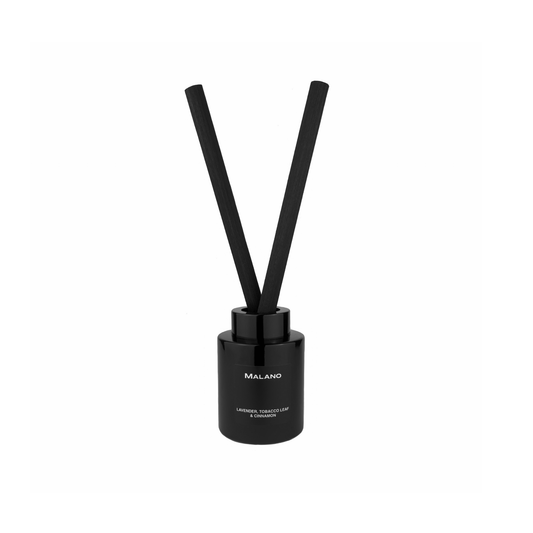 A black reed diffuser with 2 thick, long,  reeds inserted into a cylindrical glass container with a label of the brand ‘Malano’ and the scent of ‘Lavender, Tobacco Leaf and Cinnamon’ on it.