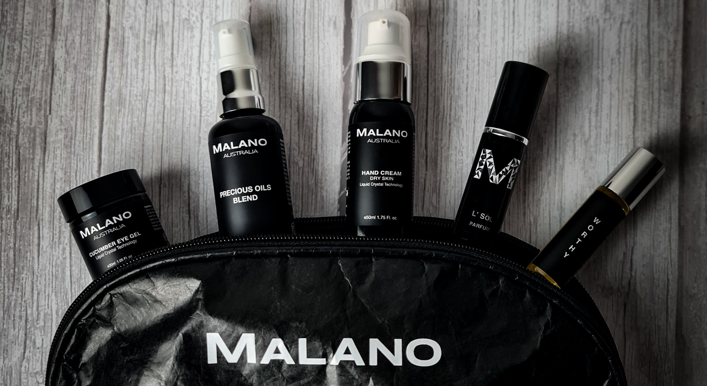 Skincare Cosmetic Bag by Malano open with a variety of Malano products coming out of it whilst laying softly lit on a light wooden surface.
