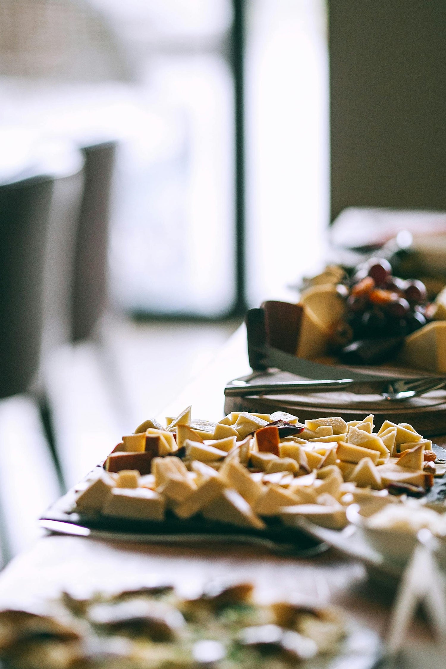 A table half out of focus with catered food for an event with chairs and a window on the left side of  the scene blurred out.