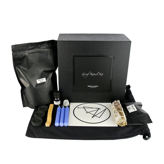A Grief Positive Intention Ritual Kit by Malano with it’s box and contents layed out in a tidy and organised manner including a bag of Himalayan Pink Salt, Anointing Oil, Charcoal, a stick of Palo Santo, three pale blue candles, a gem stone, grief sigil, lavender and sage smudge stick and Grief Resin. These elements are sitting ontop of a black drawstring bag and against a white background.