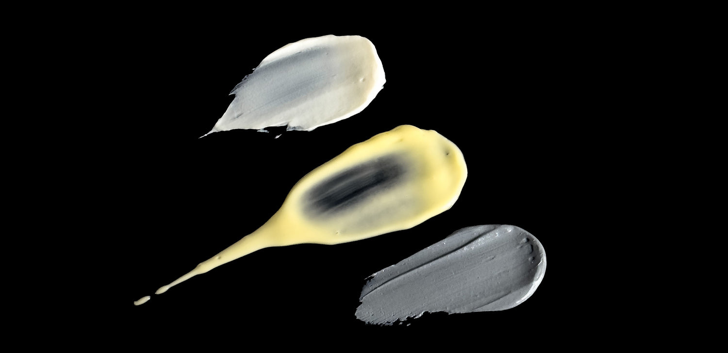 3 organic skincare swatches by Malano, one cream coloured, one yellow coloured and one grey coloured, softly illuminated against a dark background