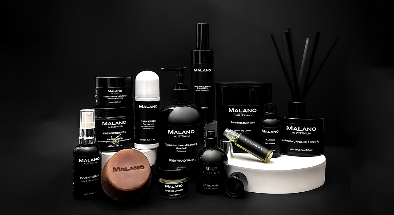 An array of luxury organic, hand made products by Malano sitting in a display arrangement softly lit from the front agains a dark grey and black background