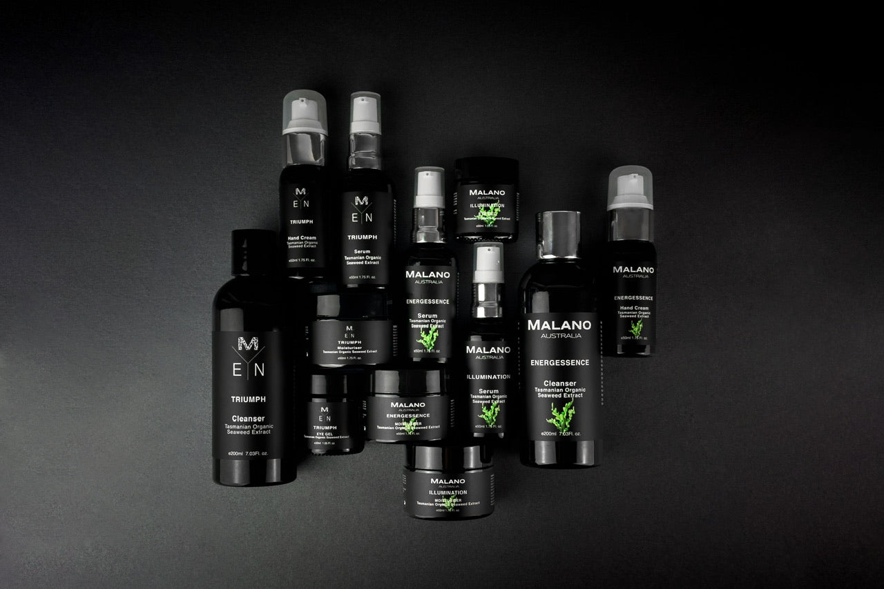 Malano’s range of Organic Tasmanian Seaweed products including mens skincare and women’s skincare, all laying side by side together on a dark grey background and softly lit from the left side. 