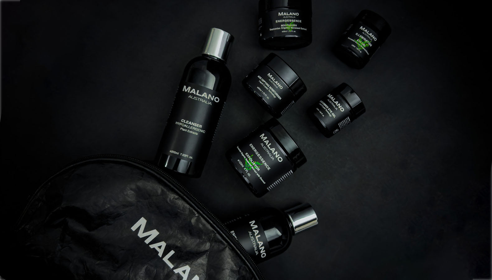Various Malano organic skincare products including eye gel, cleanser, moisturiser and exfoliator, lightly lit, spilling out of a cosmetic bag and scattered across a black background