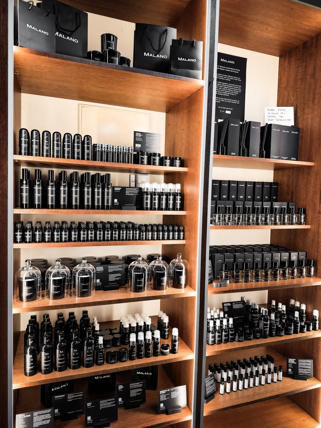 Wooden display shelves at Norman and Dann, stocked with numerous black and white Malano personal care and grooming products, including bottles, jars, and boxes.