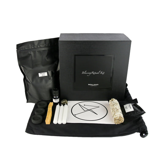 A Blessing Positive Intention Ritual Kit by Malano with it’s box and contents layed out in a tidy and organised manner including a bag of Himalayan Pink Salt, Anointing Oil, Charcoal, a stick of Palo Santo, three white candles, a gem stone, blessing sigil, sage smudge stick and Blessing Resin. These elements are sitting ontop of a black drawstring bag and against a white background.