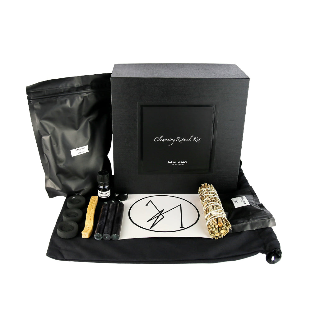 A Cleansing Positive Intention Ritual Kit by Malano with it’s box and contents layed out in a tidy and organised manner including a bag of Grey Sea Salt, Anointing Oil, Charcoal, a stick of Palo Santo, three Black Candles, a gem stone, Cleansing sigil, Mugwort/Sage smudge stick and Cleansing Resin. These elements are sitting ontop of a black drawstring bag and against a white background.