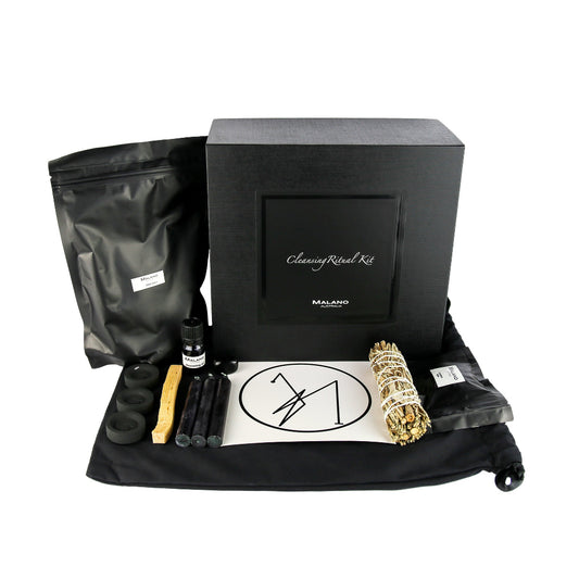 A Cleansing Positive Intention Ritual Kit by Malano with it’s box and contents layed out in a tidy and organised manner including a bag of Grey Sea Salt, Anointing Oil, Charcoal, a stick of Palo Santo, three Black Candles, a gem stone, Cleansing sigil, Mugwort/Sage smudge stick and Cleansing Resin. These elements are sitting ontop of a black drawstring bag and against a white background.
