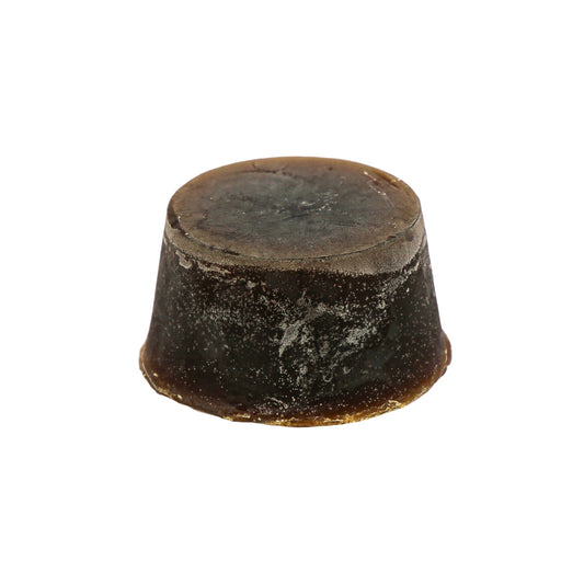 A round block of Lime, Mango and Cedarwood scented soap, with a dark brown colour and a textured surface.